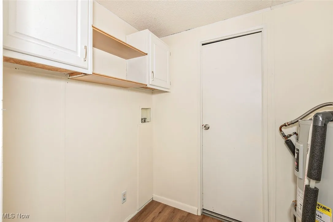 Washroom featuring cabinet space, light wood-style floors, a textured ceiling, and electric water heater
