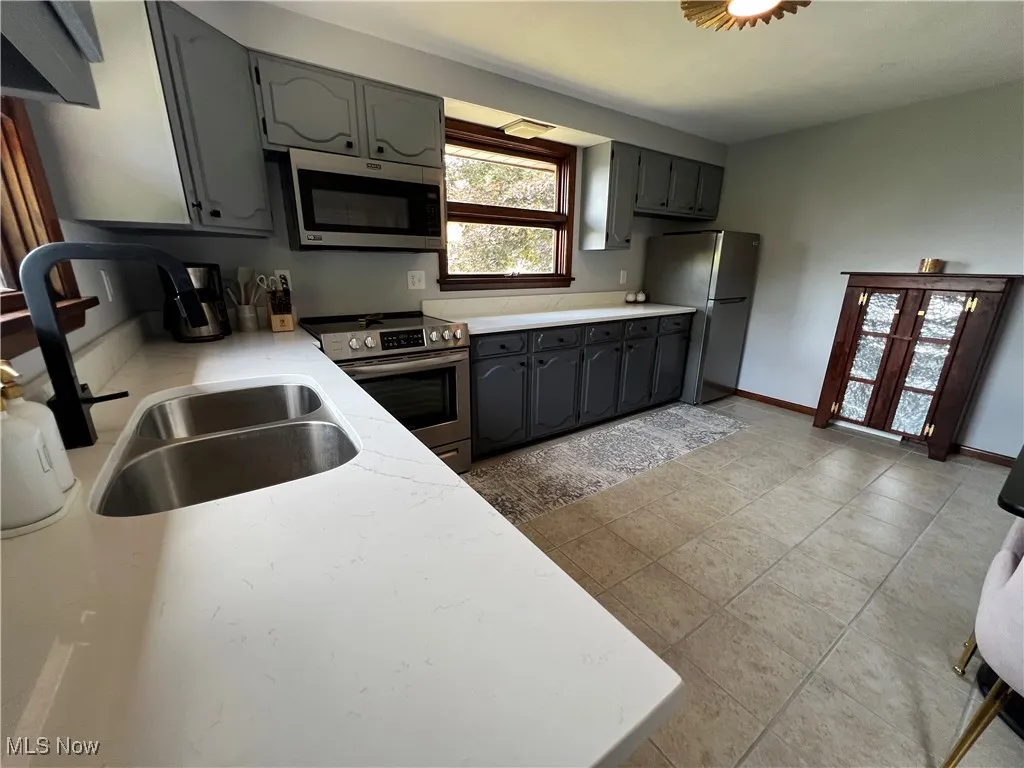 Kitchen with appliances with stainless steel finishes, gray cabinetry, and light countertops
