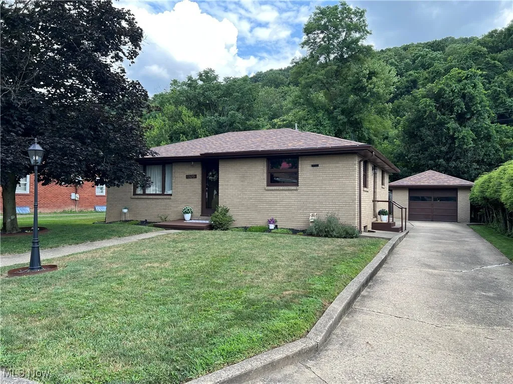 Ranch-style house with an outbuilding, a detached garage, brick siding, a front lawn, and concrete driveway