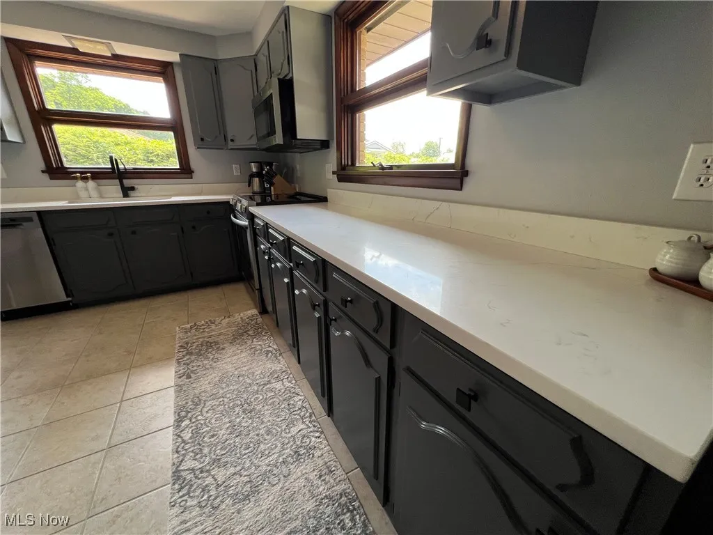 Kitchen with appliances with stainless steel finishes, light tile patterned floors, light countertops, and gray cabinets