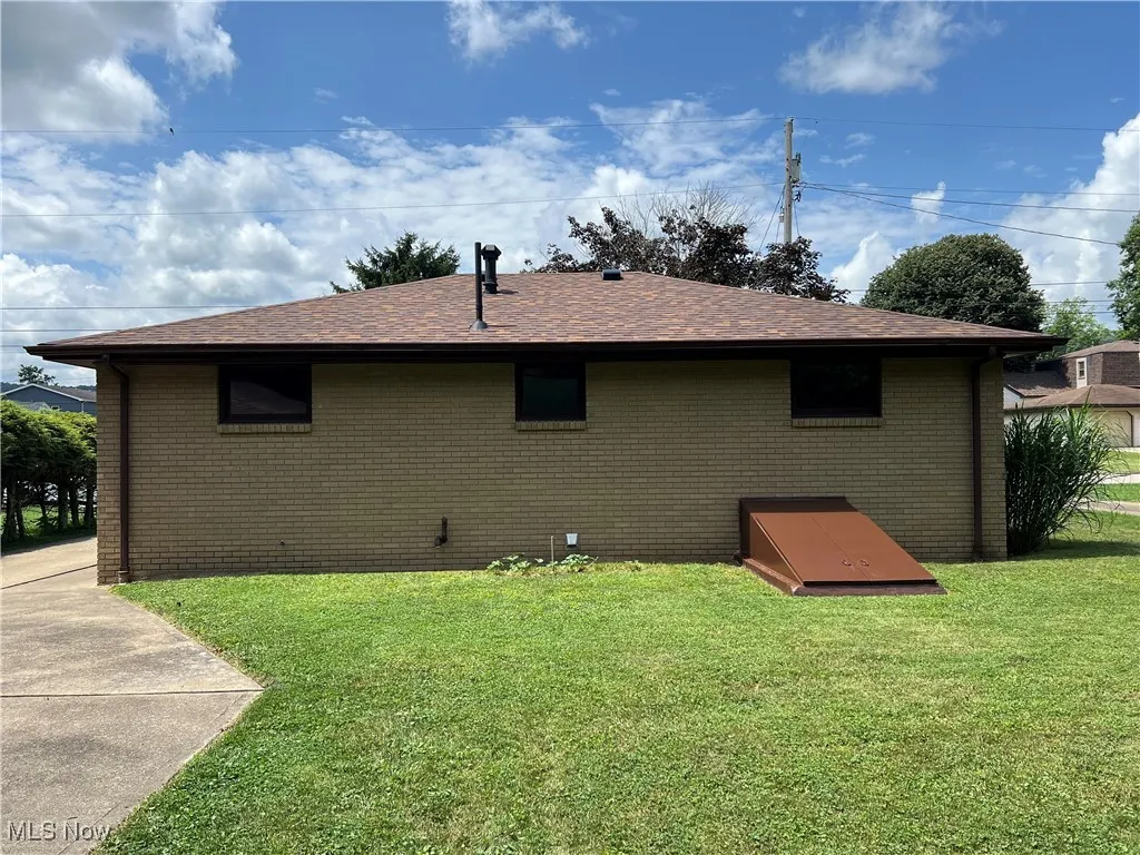 Rear view of house featuring a yard, brick siding, and roof with shingles