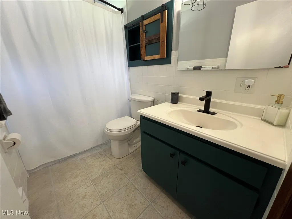 Bathroom featuring vanity, tile walls, a shower with curtain, and wainscoting
