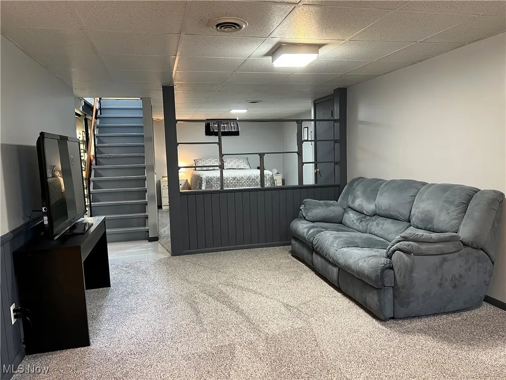 Carpeted living room featuring a drop ceiling and stairs