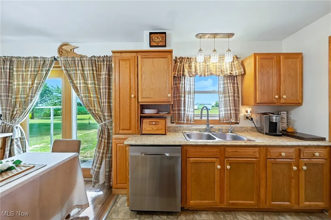 Kitchen featuring dishwasher, healthy amount of natural light, brown cabinets, and decorative light fixtures