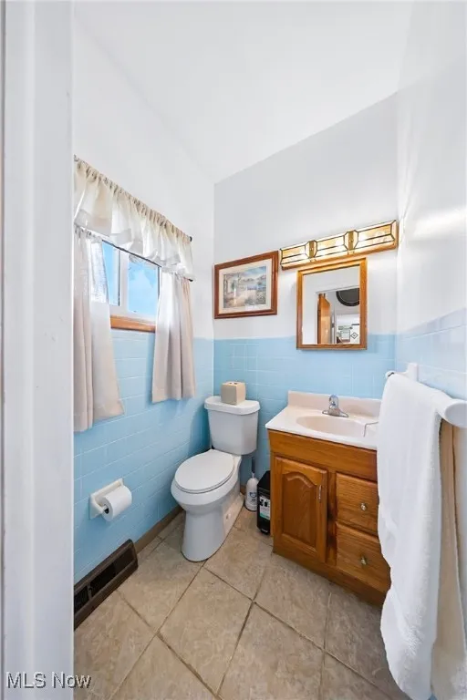 Half bath featuring tile walls, vanity, tile patterned flooring, and a wainscoted wall