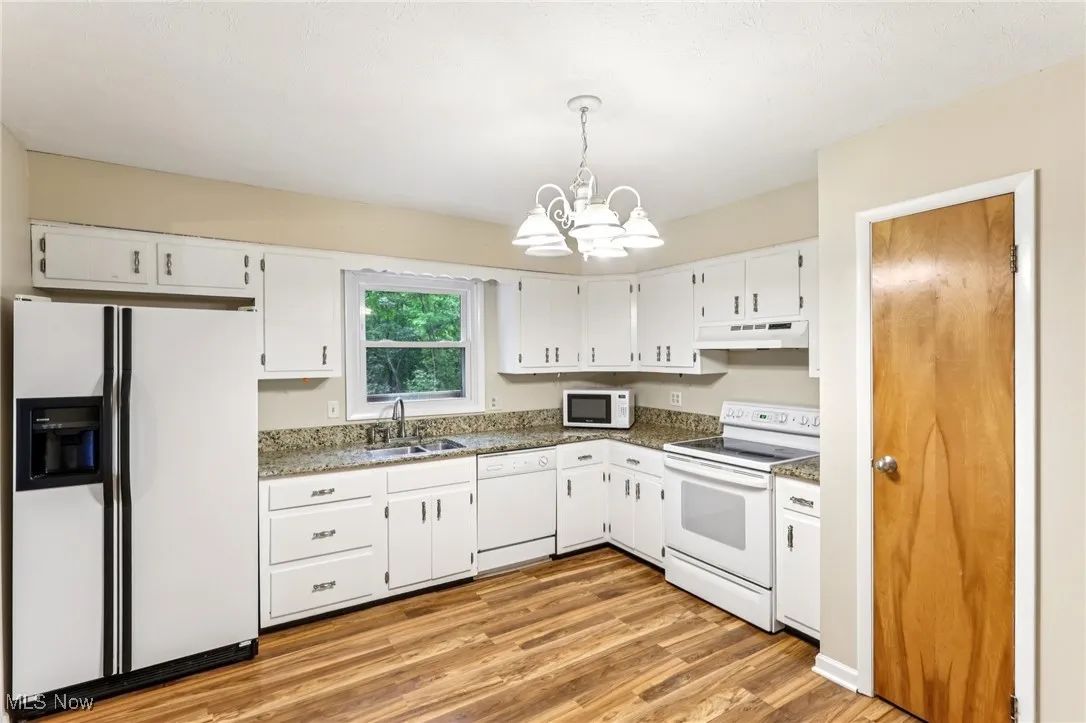 Kitchen featuring white appliances, under cabinet range hood, a chandelier, white cabinetry, and light wood-type flooring