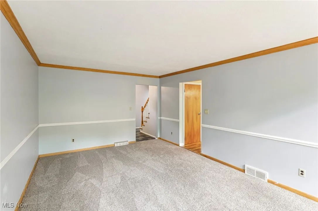 Empty room featuring carpet floors, ornamental molding, and stairs