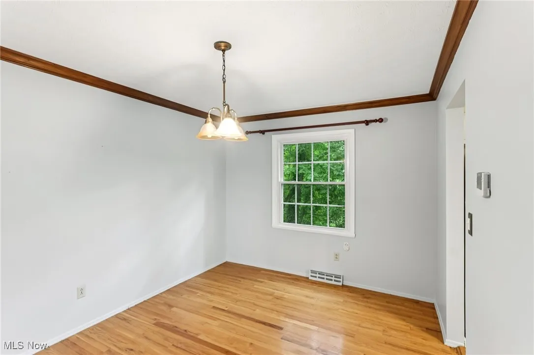 Empty room with crown molding, a chandelier, and light wood-style floors