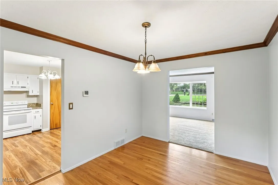 Spare room featuring a chandelier, crown molding, and light wood-type flooring