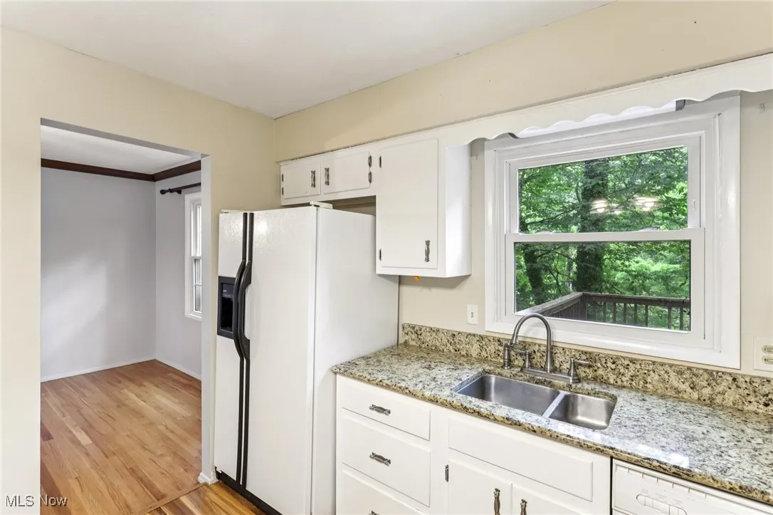 Kitchen with white appliances, light wood-type flooring, white cabinets, and light stone counters