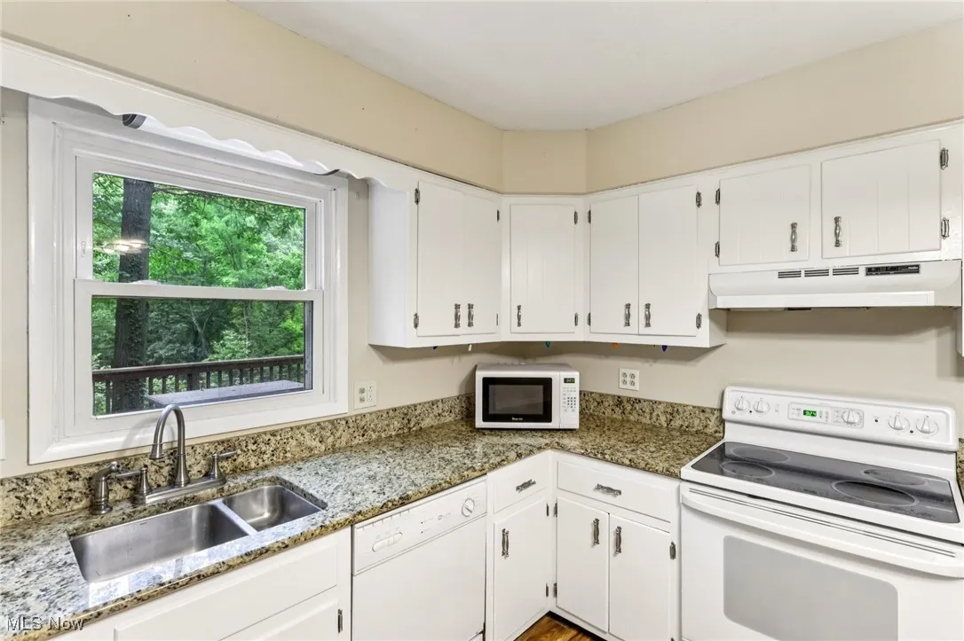 Kitchen featuring under cabinet range hood, white appliances, white cabinets, and light stone counters