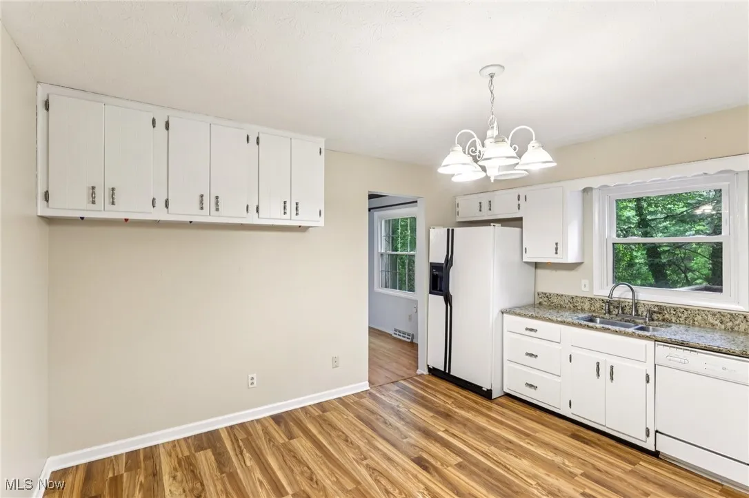 Kitchen with white appliances, a chandelier, plenty of natural light, and white cabinets