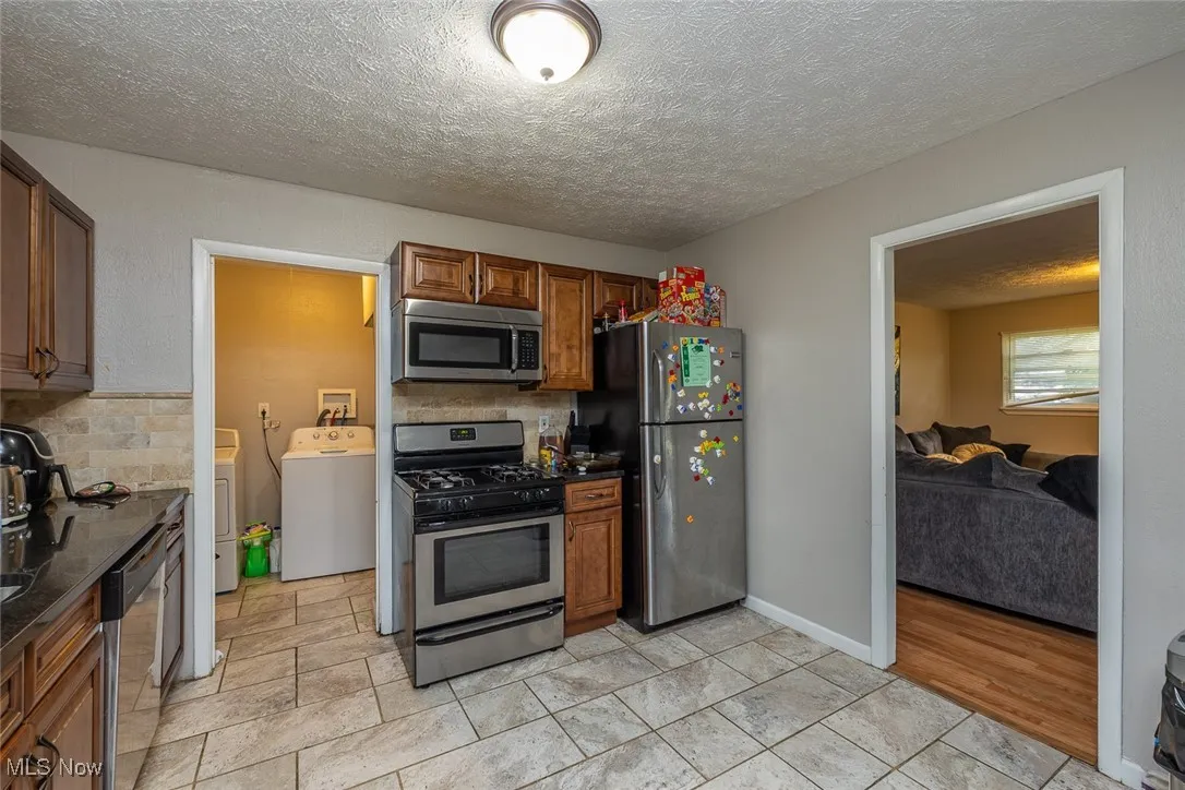 Kitchen featuring appliances with stainless steel finishes, washing machine and clothes dryer, dark countertops, decorative backsplash, and a textured ceiling