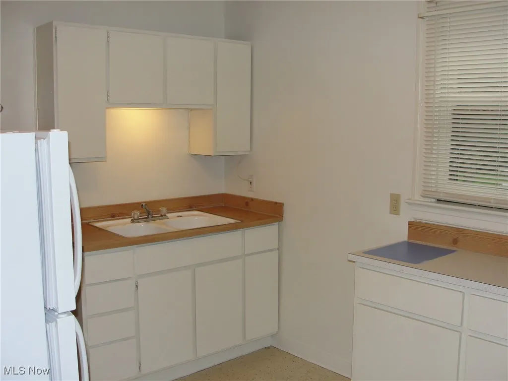 Kitchen featuring freestanding refrigerator, white cabinets, and light countertops