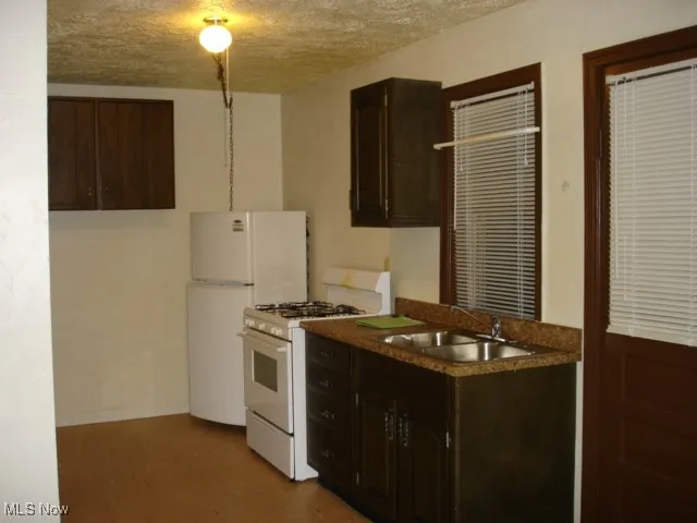 Kitchen with white appliances, dark brown cabinetry, and a textured ceiling
