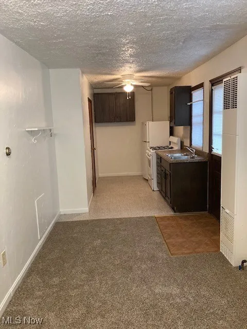 Kitchen featuring a heating unit, range, ceiling fan, a textured ceiling, and light colored carpet