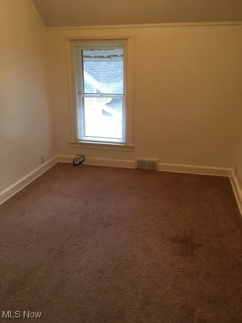 Unfurnished room featuring dark colored carpet and baseboards
