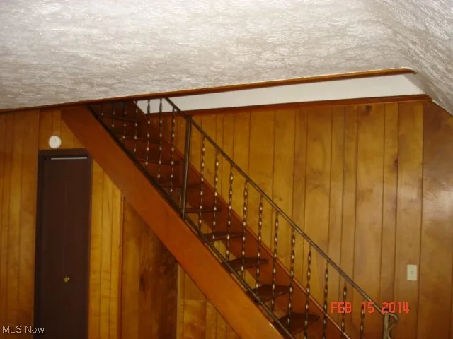 Staircase featuring wood walls and a textured ceiling