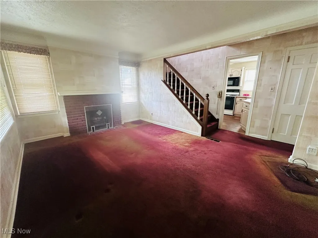 Unfurnished living room with stairway, a brick fireplace, dark colored carpet, and a textured ceiling