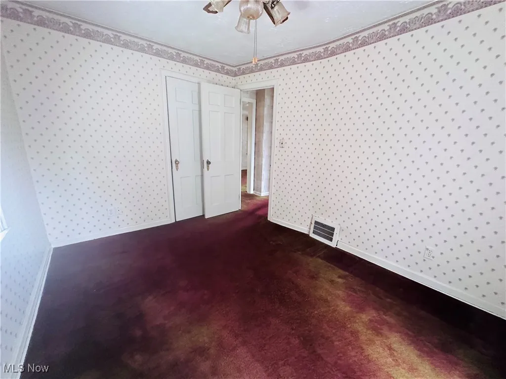 Unfurnished bedroom featuring wallpapered walls, dark colored carpet, and ceiling fan
