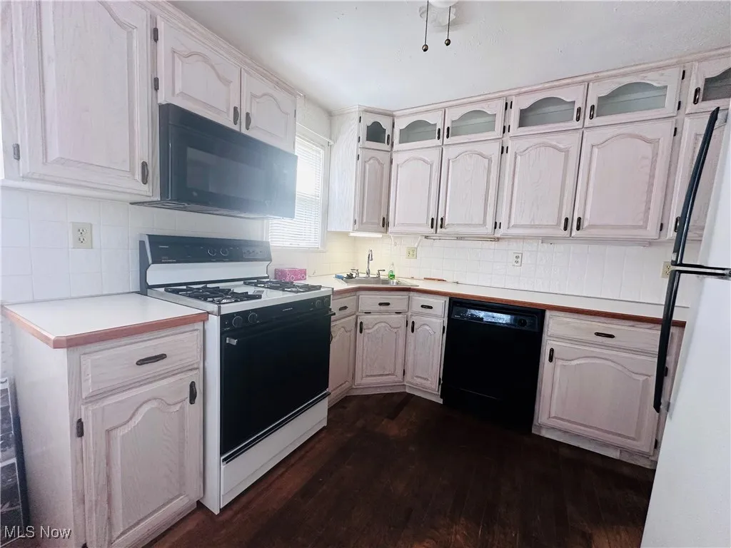 Kitchen featuring black appliances, dark wood finished floors, light countertops, tasteful backsplash, and glass insert cabinets