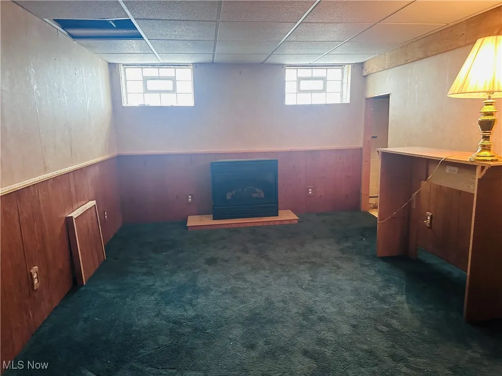 Below grade area with healthy amount of natural light, carpet, wooden walls, and a drop ceiling