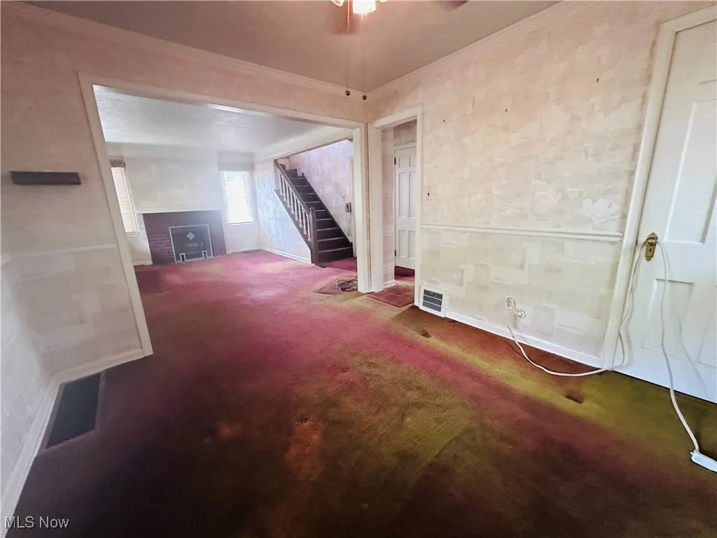 Unfurnished living room with stairs, carpet, a fireplace, ornamental molding, and ceiling fan