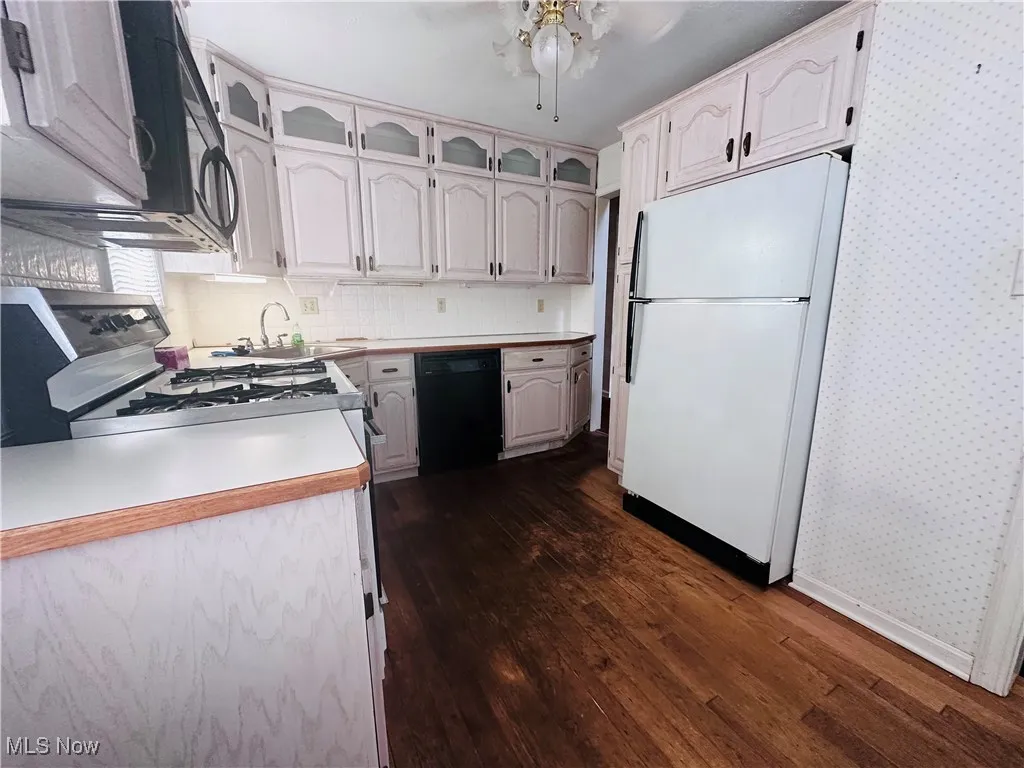Kitchen featuring freestanding refrigerator, dishwasher, wallpapered walls, dark wood-type flooring, and glass insert cabinets