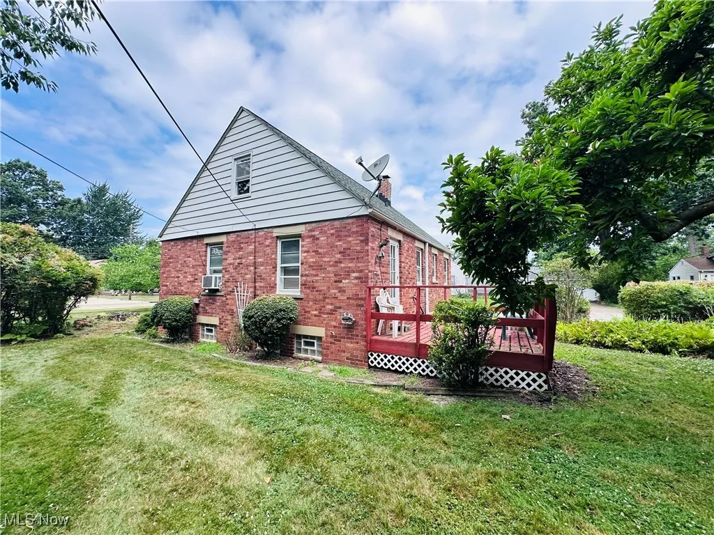 View of home's exterior with brick siding, a deck, a lawn, and a chimney
