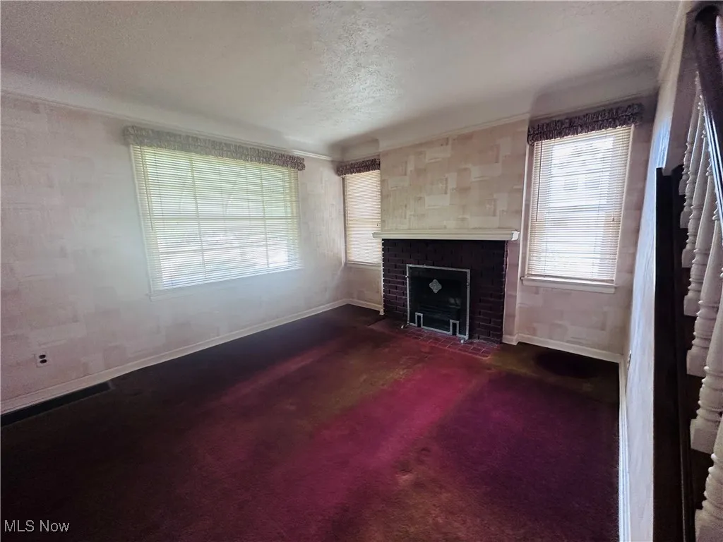 Unfurnished living room with a textured ceiling, a brick fireplace, and dark colored carpet