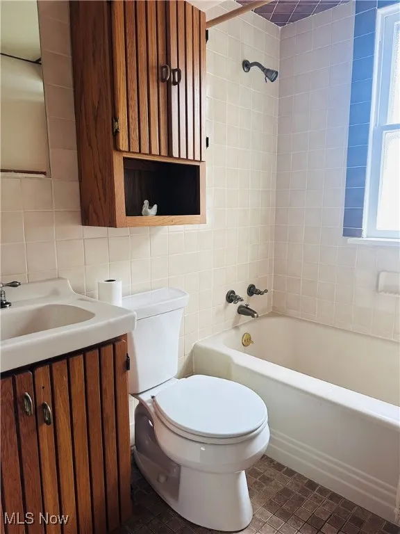 Bathroom with tile walls, vanity, and shower / bathtub combination