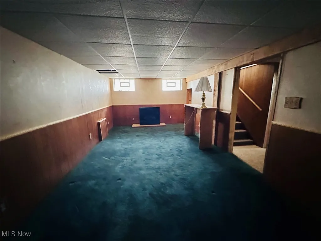 Below grade area with a paneled ceiling, carpet floors, wainscoting, stairway, and wooden walls