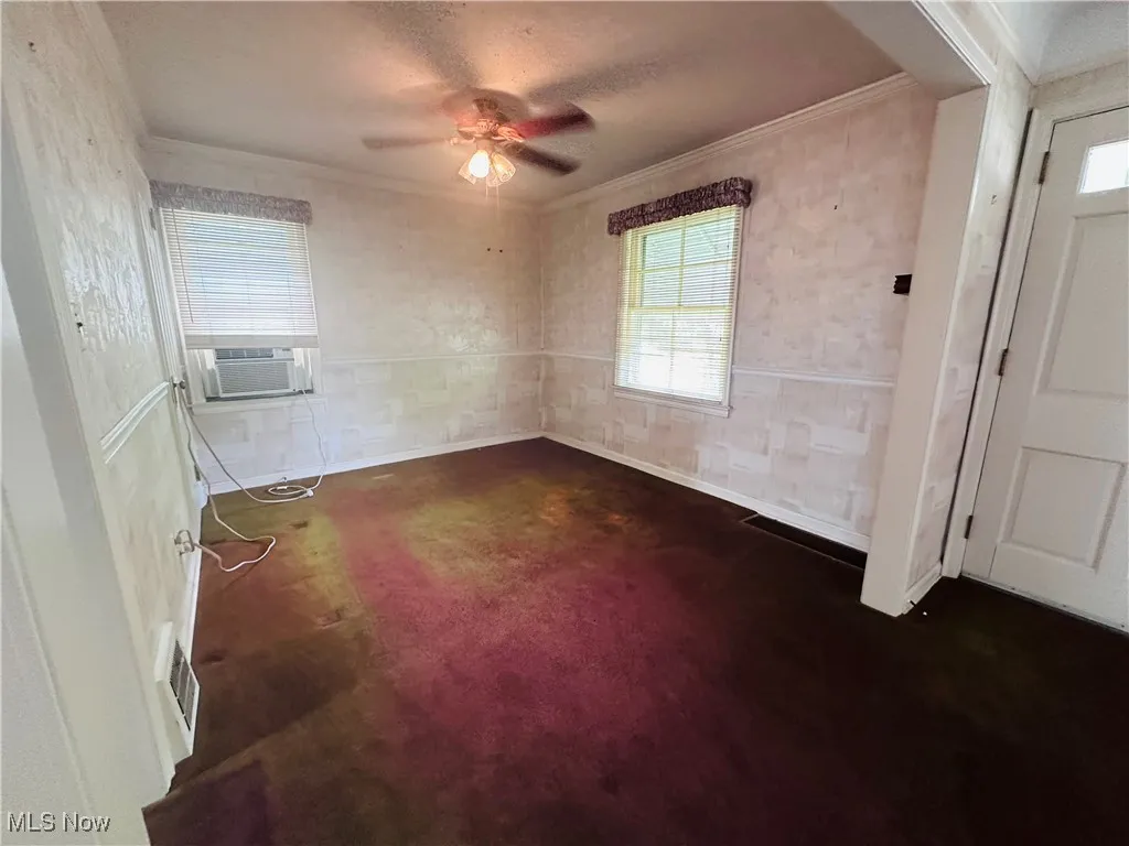 Empty room with ornamental molding, cooling unit, a ceiling fan, and dark colored carpet