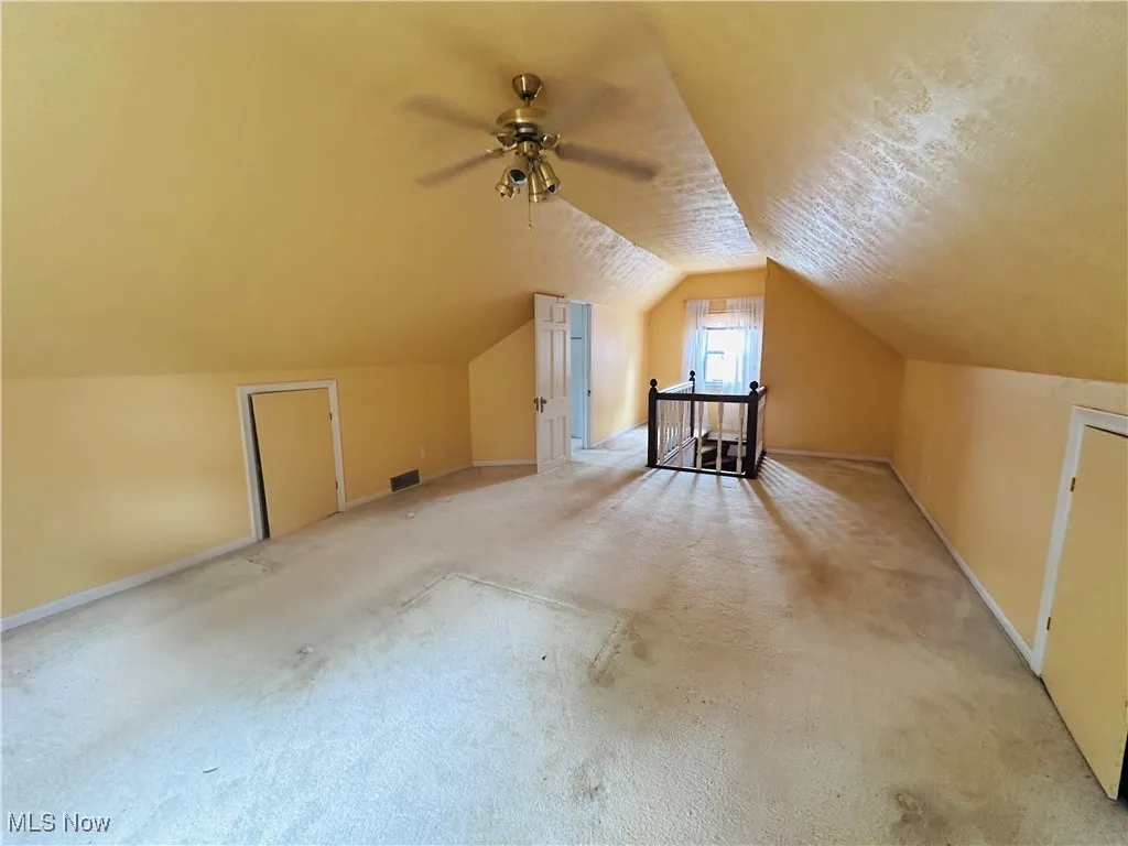 Additional living space with light colored carpet, a ceiling fan, and vaulted ceiling