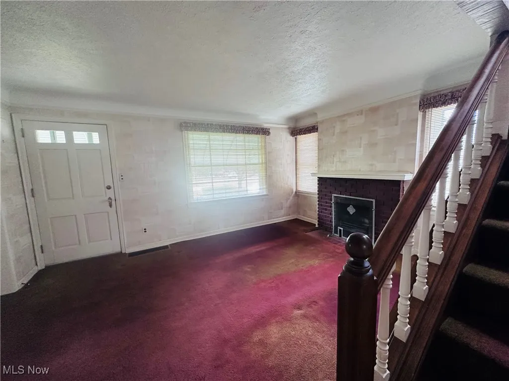 Unfurnished living room with a textured ceiling, a fireplace, carpet, and plenty of natural light