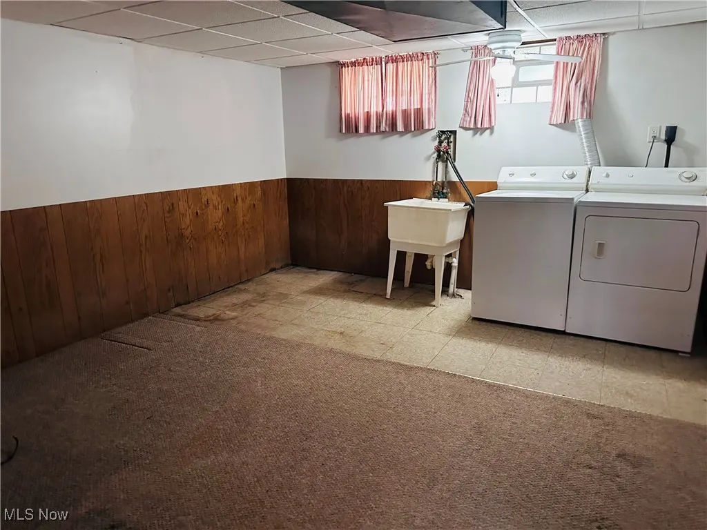 Basement featuring separate washer and dryer, wainscoting, a paneled ceiling, wooden walls, and light floors