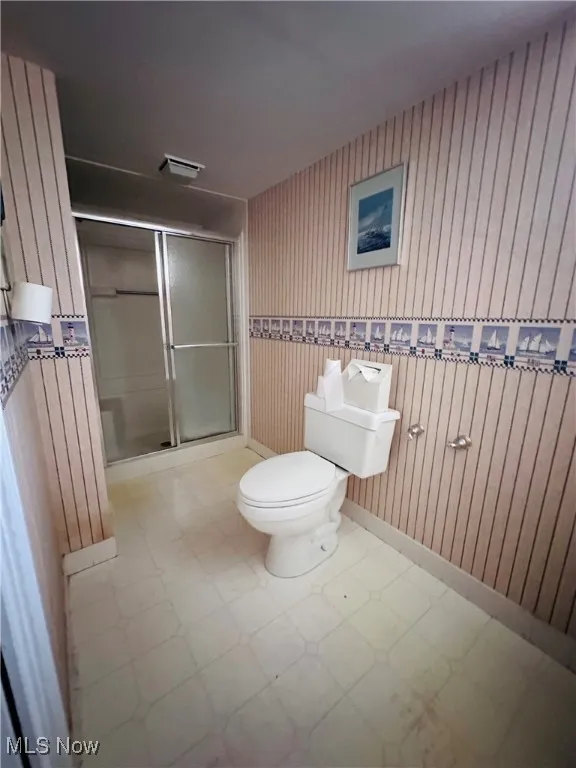 Full bath with tile patterned floors, a stall shower, and wood walls