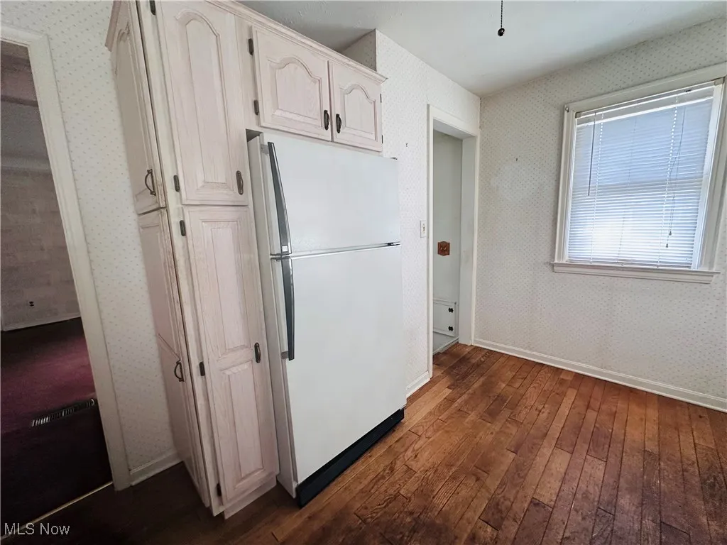 Kitchen featuring freestanding refrigerator, wallpapered walls, dark wood-style flooring, and white cabinetry
