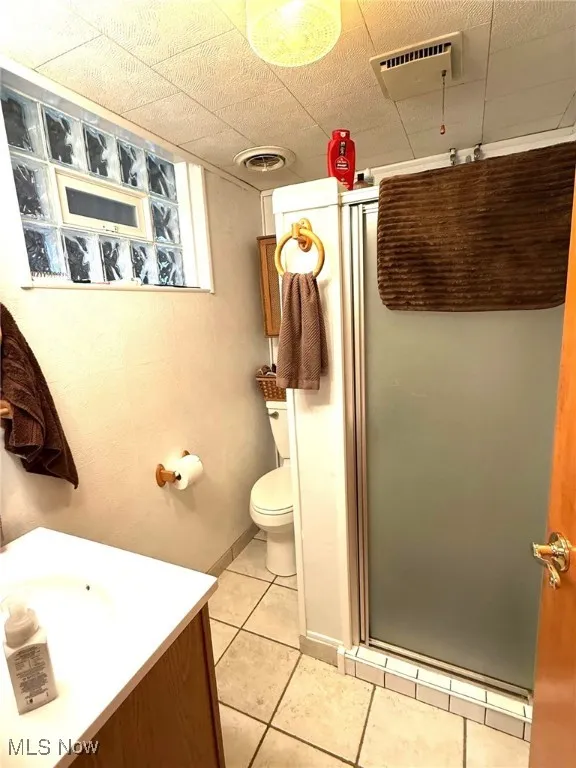 Bathroom featuring a stall shower, tile patterned flooring, vanity, and toilet