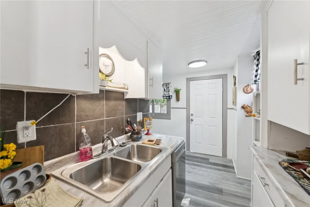 Kitchen with white cabinets, light wood-type flooring, decorative backsplash, and light countertops