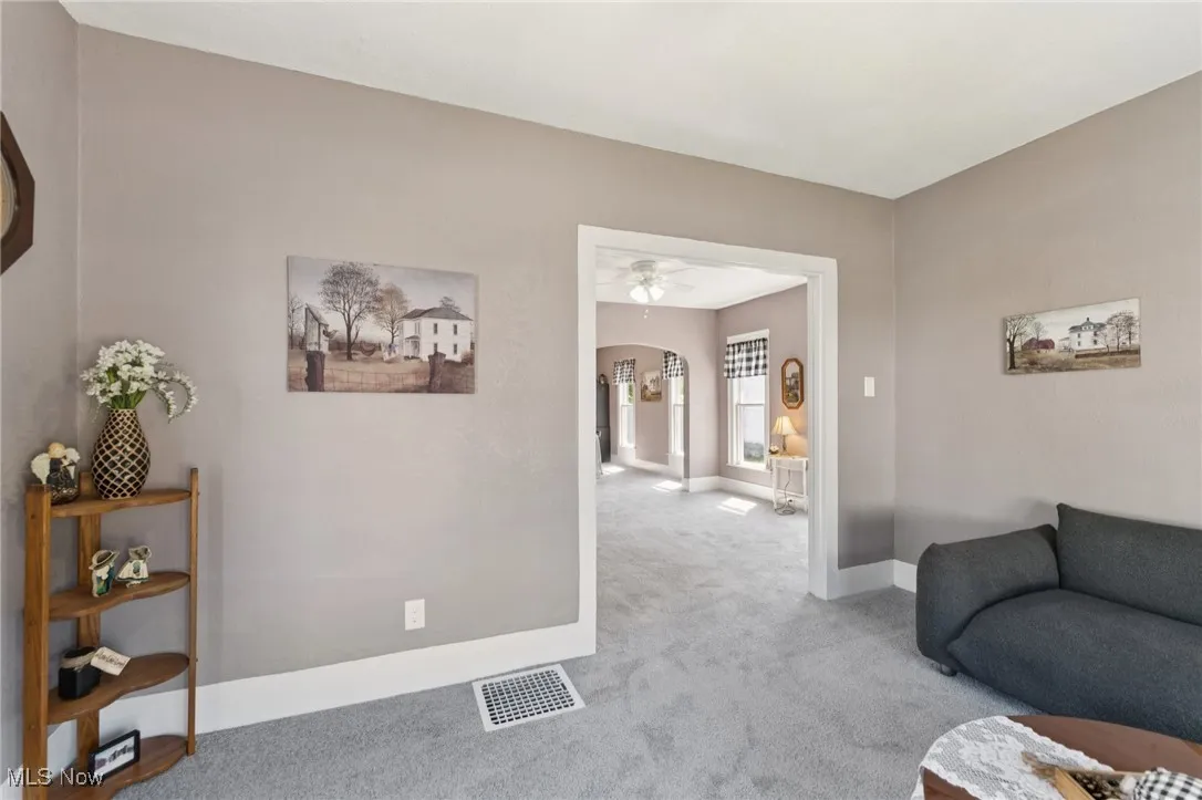 Carpeted living area featuring arched walkways and ceiling fan