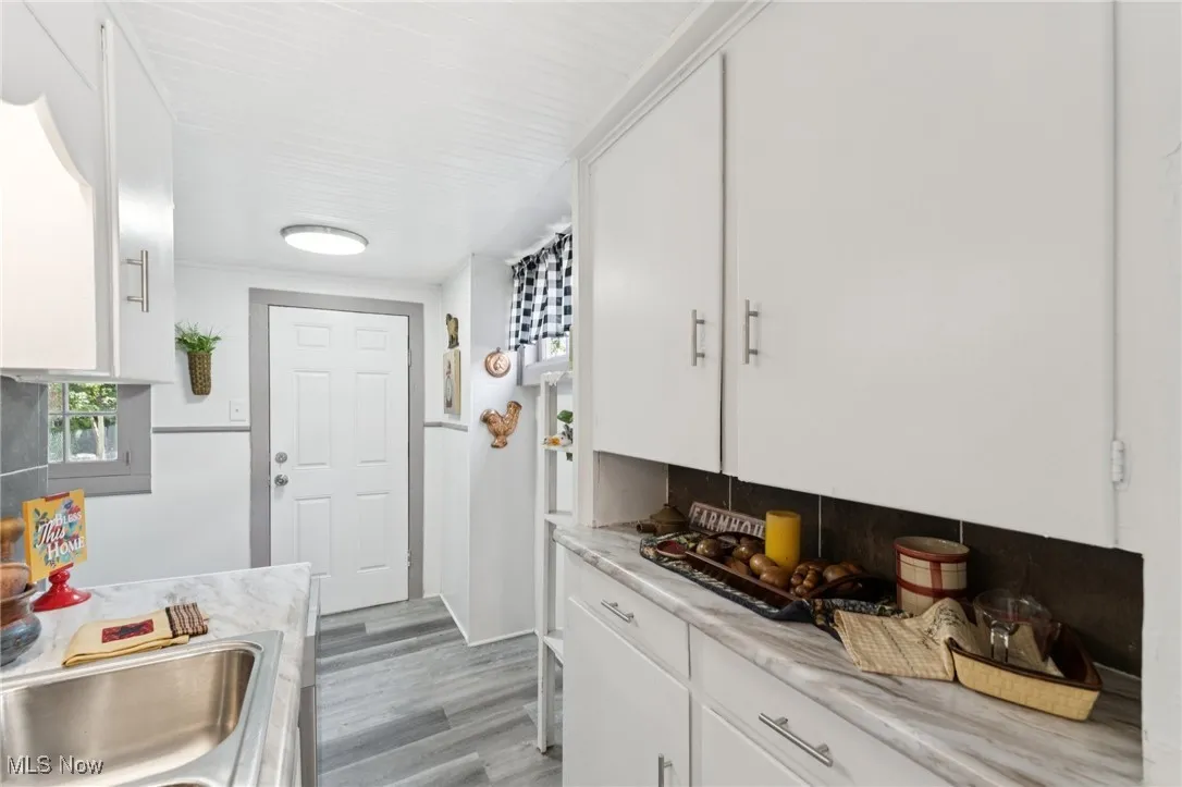 Kitchen featuring light wood finished floors, white cabinetry, light countertops, and decorative backsplash