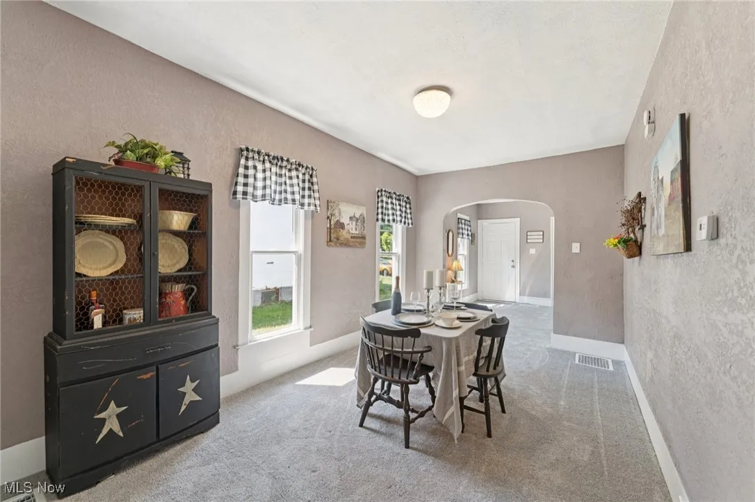 Dining room with arched walkways, a textured wall, and carpet floors