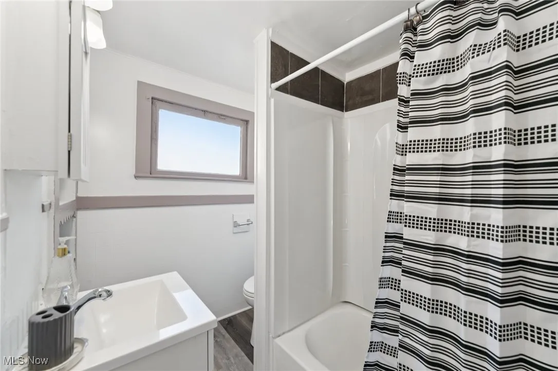 Bathroom with wood finished floors, shower / tub combo with curtain, and vanity