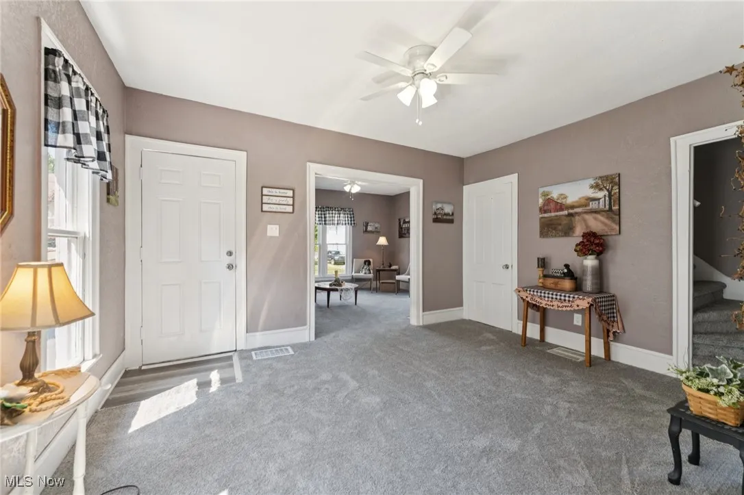 Foyer entrance featuring ceiling fan and carpet floors
