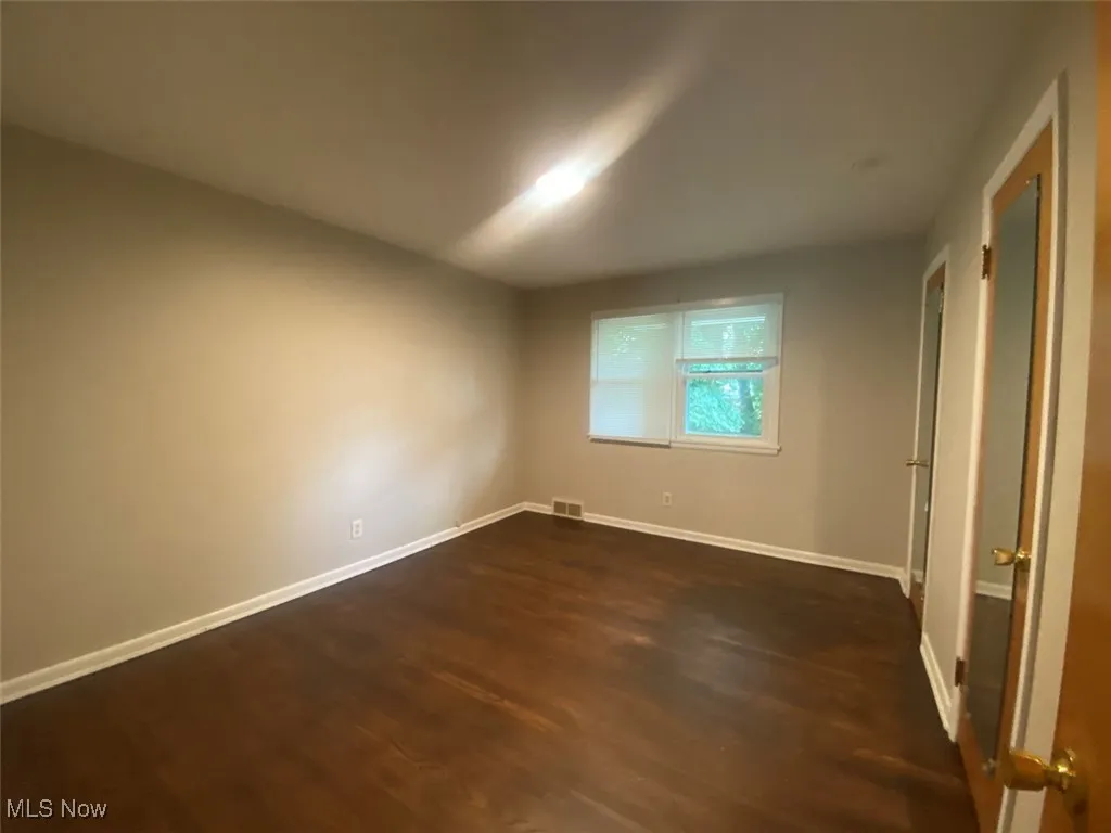 Unfurnished room with baseboards and dark wood-type flooring