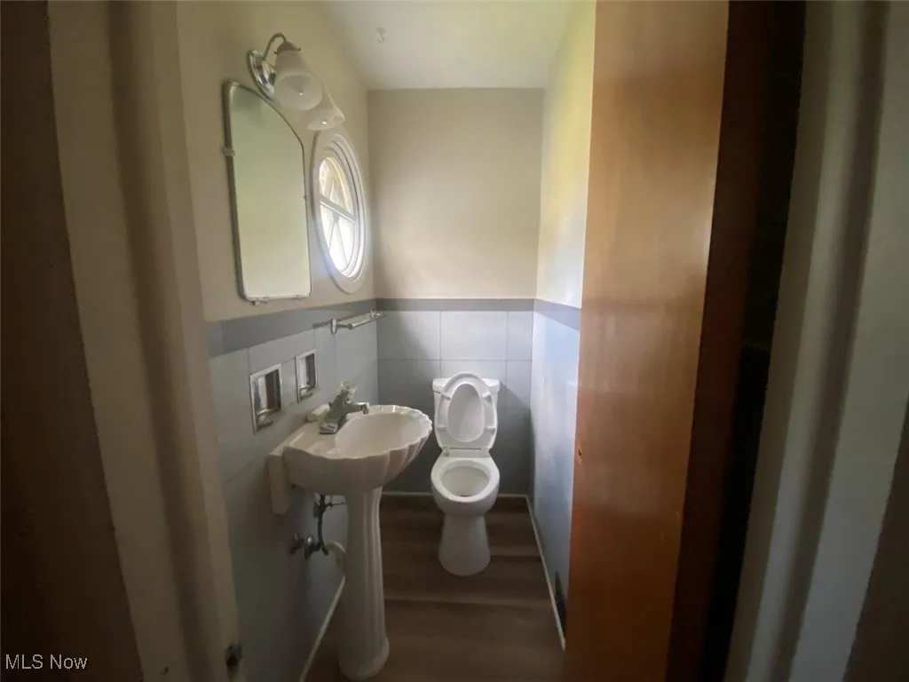 Bathroom with wood finished floors, wainscoting, and tile walls