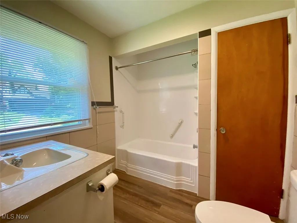 Bathroom featuring wood finished floors, bathing tub / shower combination, vanity, and tile walls