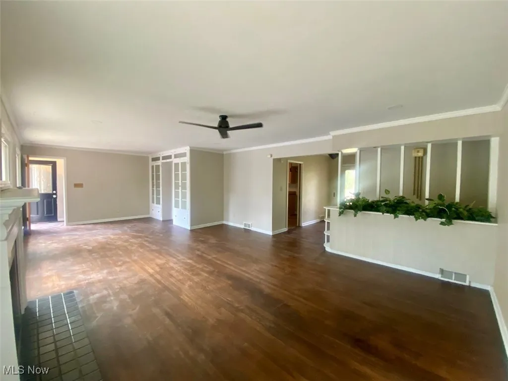 Unfurnished living room with crown molding, ceiling fan, dark wood-style floors, and a fireplace