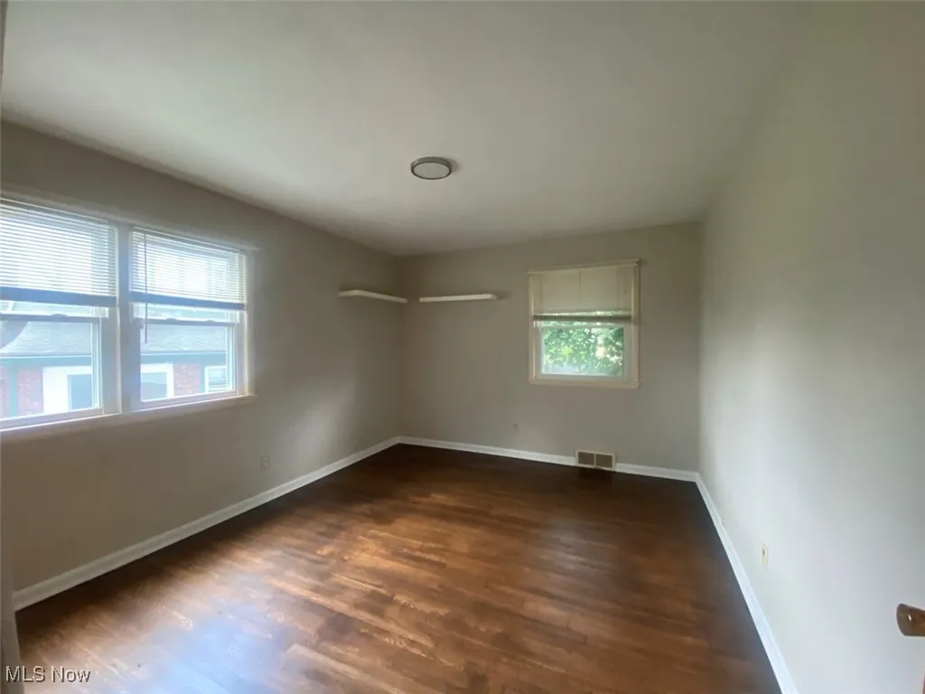 Spare room with dark wood-type flooring and baseboards